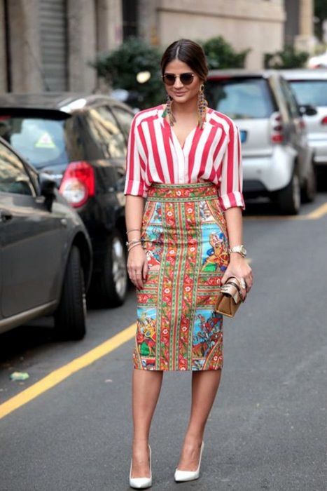 Chica usando una falda estampada con colores y un top de líneas rojas con bolso estampado y aretes de plumas